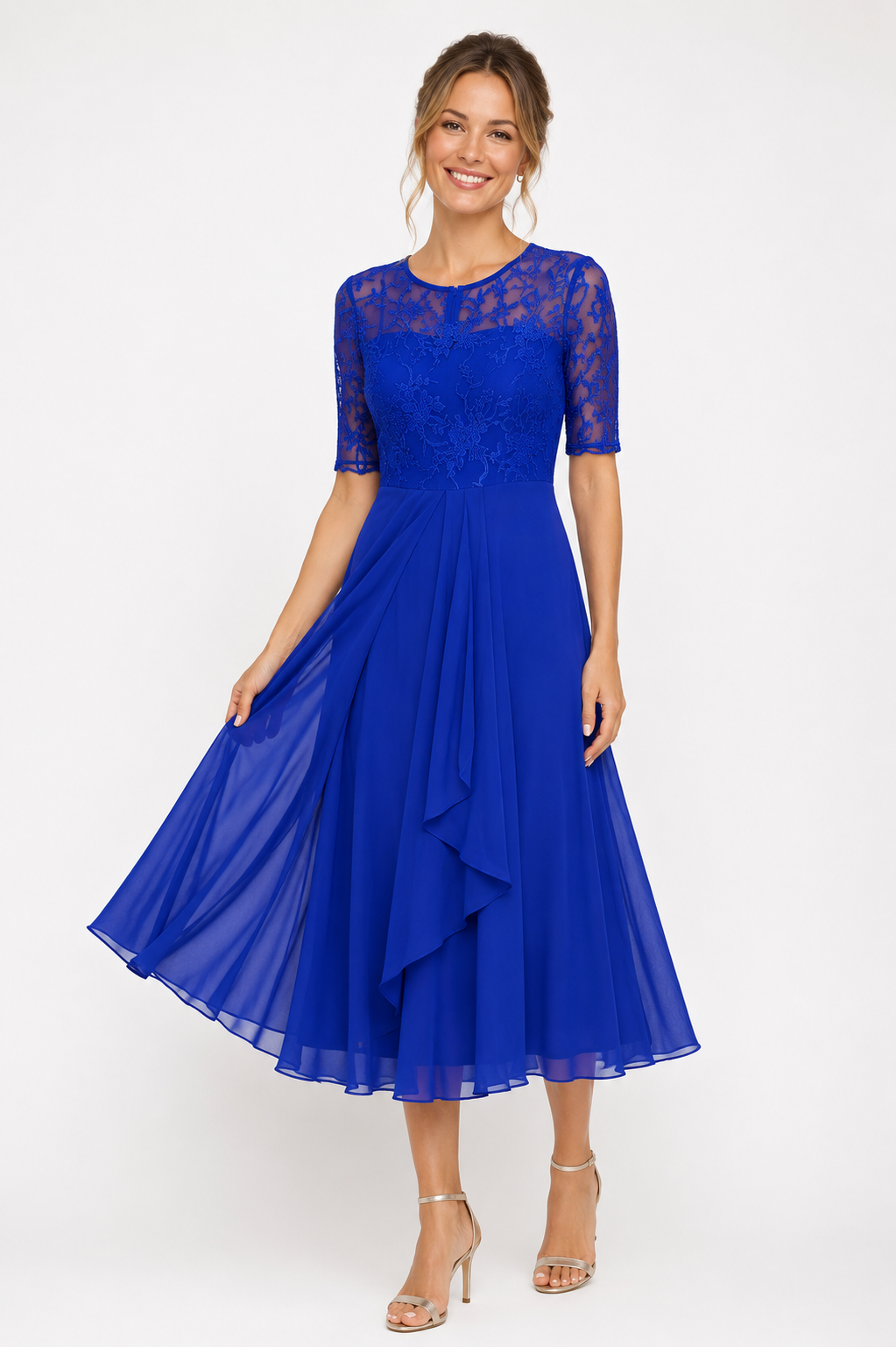 A woman modeling a royal blue midi dress with a lace bodice, short sleeves, and a flowing ruffled skirt, photographed against a plain light gray studio background.