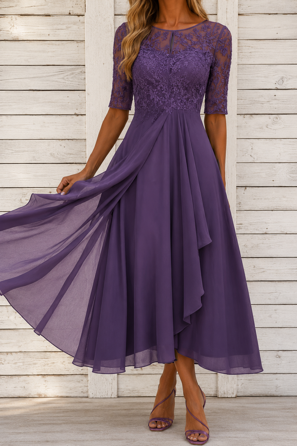 A woman wearing a purple midi dress with a lace bodice, sheer elbow-length sleeves, and a flowing chiffon skirt, standing against a white wooden plank wall.